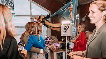 Two women are hugging and taking a picture with the KRUU photo booth. There are also two other women in the picture.