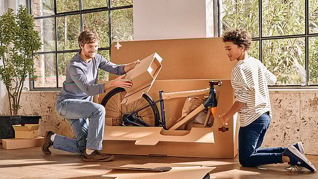 Bir baba ve oğlu bisikletin ambalajını açıyor.