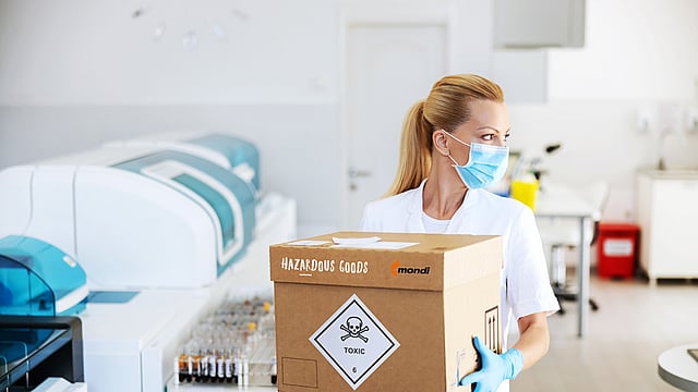 Tehlikeli madde içeren bir oluklu mukavva kutu taşıyan bir kadın.
