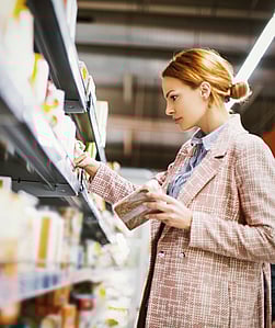 Bir kadın ayakta durmuş, süpermarket rafından bir ürün seçiyor.