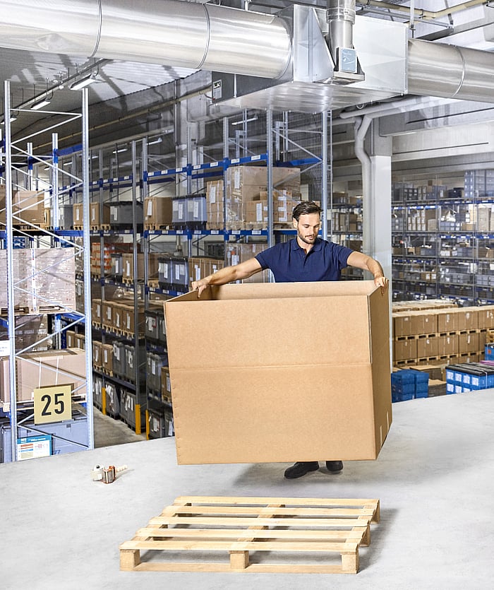 Büyük bir oluklu mukavva kutuyu kuran kişi